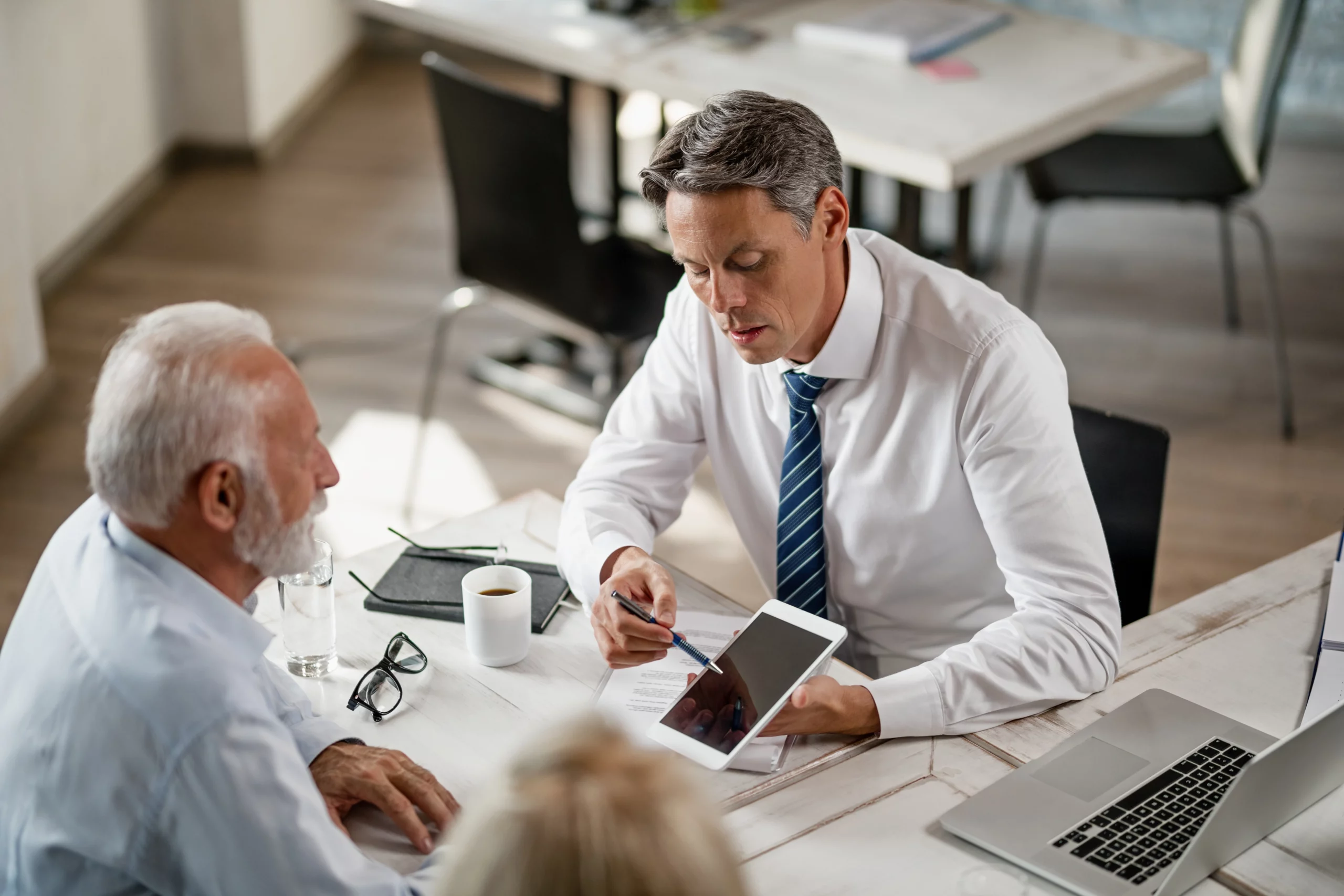 Business meeting with elder law attorney advising senior man using tablet in bright office