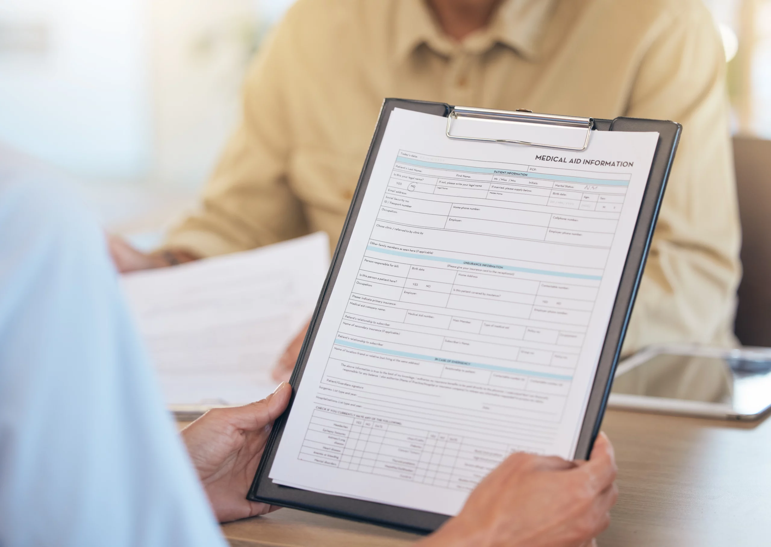 Person holding a clipboard showing a “Medical Aid Information” form while another individual reviews a paper — evoking a professional healthcare setting, careful documentation, and focused evaluation of Medicaid-benefit eligibility or medical aid planning.